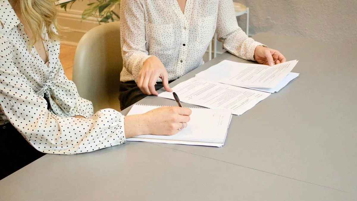 Zwei Frauen prüfen und unterzeichnen gemeinsam Vertragsunterlagen – Symbol für Mietverträge, Rechtssicherheit und die Rolle der Mietkautionsversicherung.