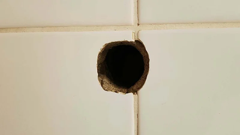 Großes Bohrloch in einer weißen Fliese – Symbolbild für Beschädigungen in Mietwohnungen und mögliche Auswirkungen auf die Rückzahlung der Mietkautionsversicherung.