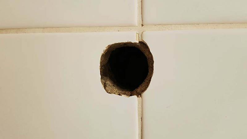 Großes Bohrloch in einer weißen Fliese – Symbolbild für Beschädigungen in Mietwohnungen und mögliche Auswirkungen auf die Rückzahlung der Mietkautionsversicherung.