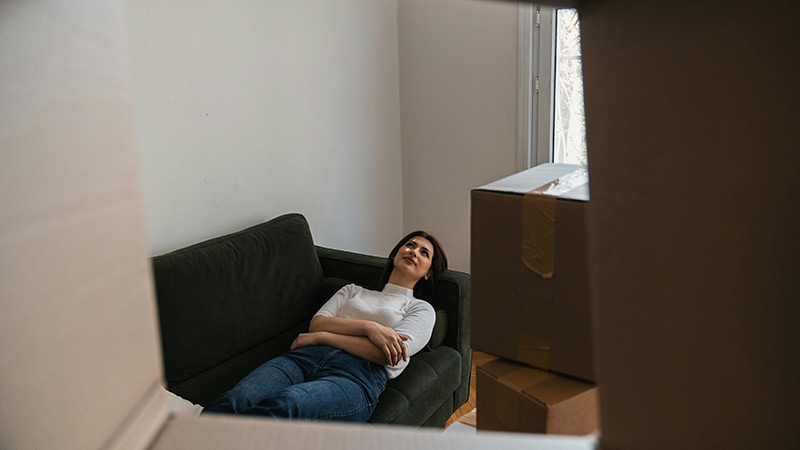 Junge Frau sitzt erschöpft auf einem Sofa zwischen Umzugskartons – Symbolbild für Wohnungswechsel, Einzug und Bedeutung der Mietkautionsversicherung beim Umzug.