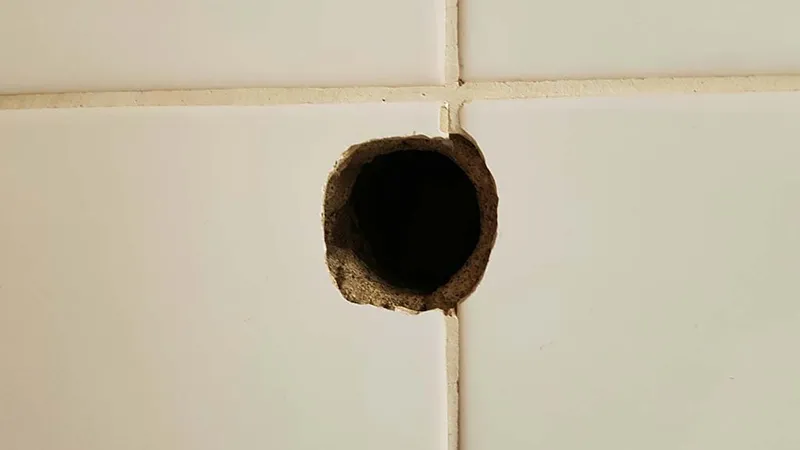 Großes Bohrloch in einer weißen Fliese – Symbolbild für Beschädigungen in Mietwohnungen und mögliche Auswirkungen auf die Rückzahlung der Mietkautionsversicherung.