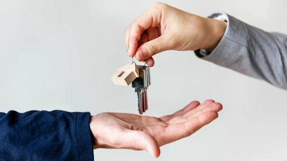 Symbolische Schlüsselübergabe zwischen zwei Personen mit einem Schlüsselbund samt Hausanhänger – typisches Motiv für Mietbeginn, Wohnungsübergabe und Absicherung durch eine Mietkautionsversicherung.