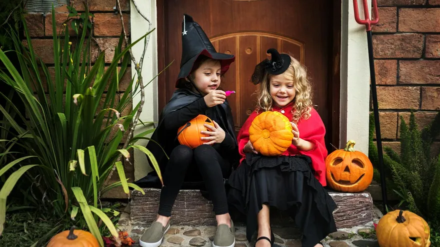 Zwei Kinder im Halloweenkostüm sitzen lachend vor einer Haustür mit Kürbissen – Symbol für Zuhause, Geborgenheit und Mietkautionsversicherung.