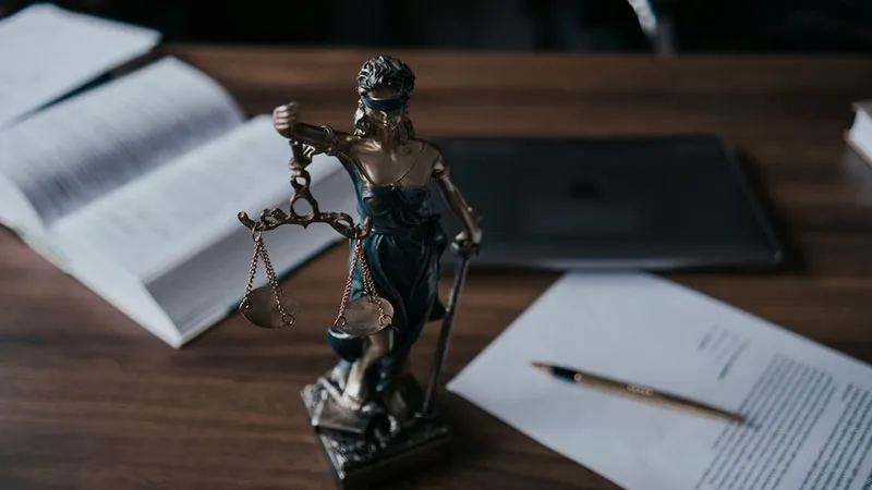 Justitia-Figur auf Schreibtisch mit Dokumenten, Gesetzbuch und Laptop – Symbolbild für rechtliche Aspekte der Mietkautionsversicherung.