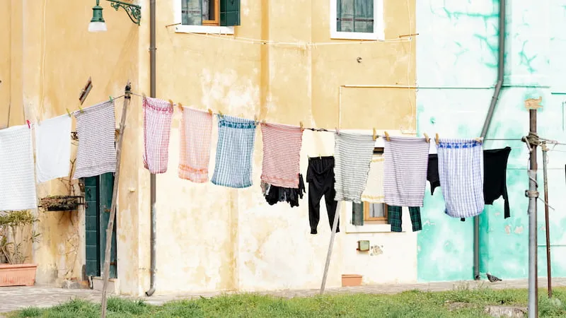 Bunte Wäsche hängt an einer Leine vor einer mediterranen Hausfassade – Symbolbild für rechtliche Fragen zur Wäschetrocknung im Mietverhältnis im Kontext einer Mietkautionsversicherung.