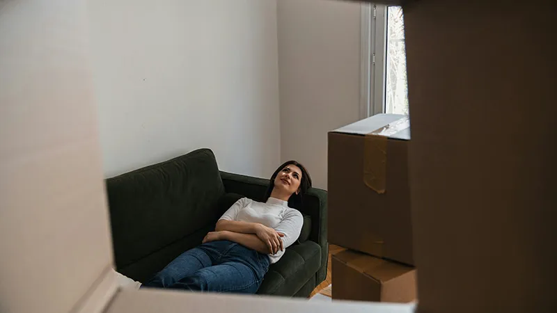 Junge Frau sitzt erschöpft auf einem Sofa zwischen Umzugskartons – Symbolbild für Wohnungswechsel, Einzug und Bedeutung der Mietkautionsversicherung beim Umzug.