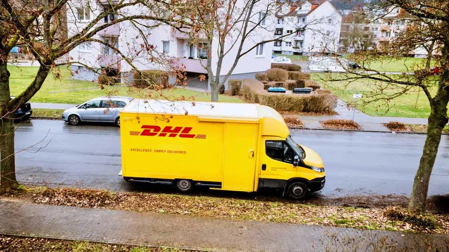 Gelber DHL-Transporter steht vor einem Wohnhaus in einer ruhigen Wohngegend – Symbol für Umzug, Zustellung und die Verbindung zur Mietkautionsversicherung.