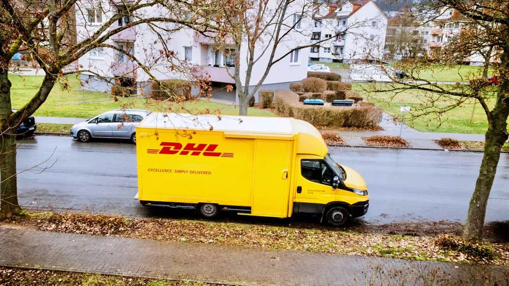 Gelber DHL-Transporter steht vor einem Wohnhaus in einer ruhigen Wohngegend – Symbol für Umzug, Zustellung und die Verbindung zur Mietkautionsversicherung.